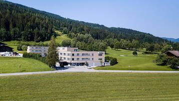 A modern building with a flat roof, surrounded by a well-maintained lawn and a forested hillside.