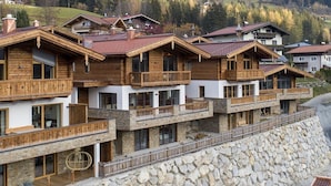 A row of wooden chalet-style buildings with balconies, set against a mountainous backdrop. - Luxury Chalet in Neukirchen near Wildkogel Ski Arena (Neukirchen am Grossvenediger)