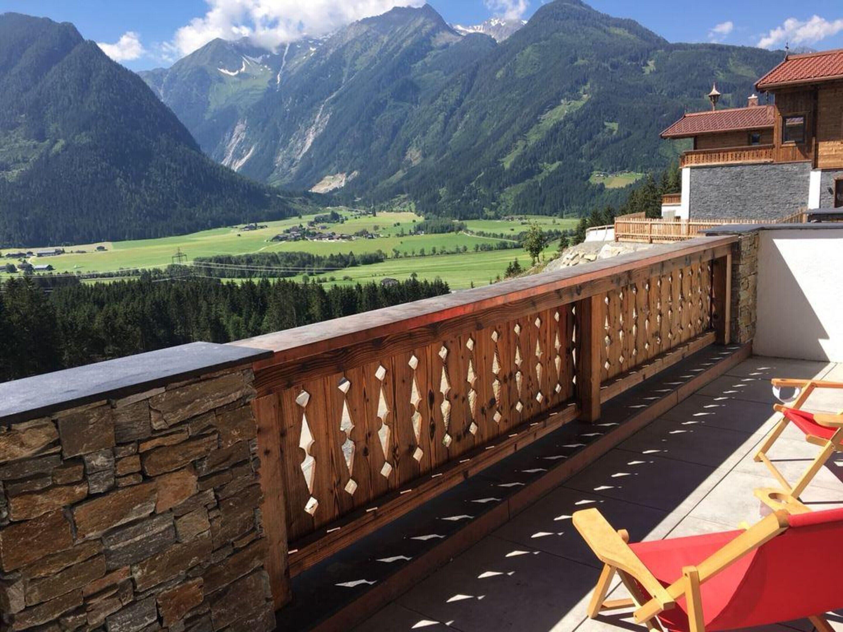 A balcony with a stone wall, wooden railing, and a view of a mountainous landscape.