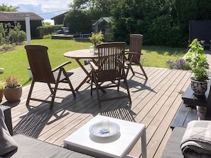 Eine Holzterrasse mit Tisch und Stühlen, umgeben von Blumentöpfen und einem Garten.