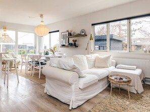 A spacious living room with a white sofa, a dining table, and a large window providing a view of the outside. - 6 Person Holiday Home in Rude (Bisserup)