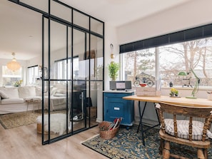 A modern living space with a glass partition, a dining area with a wooden table, and a view of trees through large windows. - 6 Person Holiday Home in Rude (Bisserup)