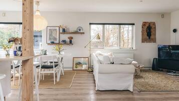 A modern living room with a white sofa, a dining table with chairs, a TV, and artwork on the walls.