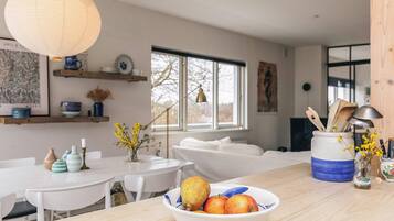 A modern kitchen with white furniture, a bowl of fruit on the counter, and a large window.