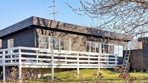 A two-story wooden house with a white deck, a satellite dish, and a ladder leaning against the house. - 6 Person Holiday Home in Rude (Bisserup)