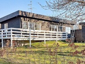 A two-story wooden house with a white deck, a satellite dish, and a ladder leaning against the house.