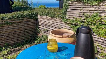 A blue table with a yellow pitcher, a black container, and a patterned cup, set against a backdrop of a wooden fence and a view of the sea.