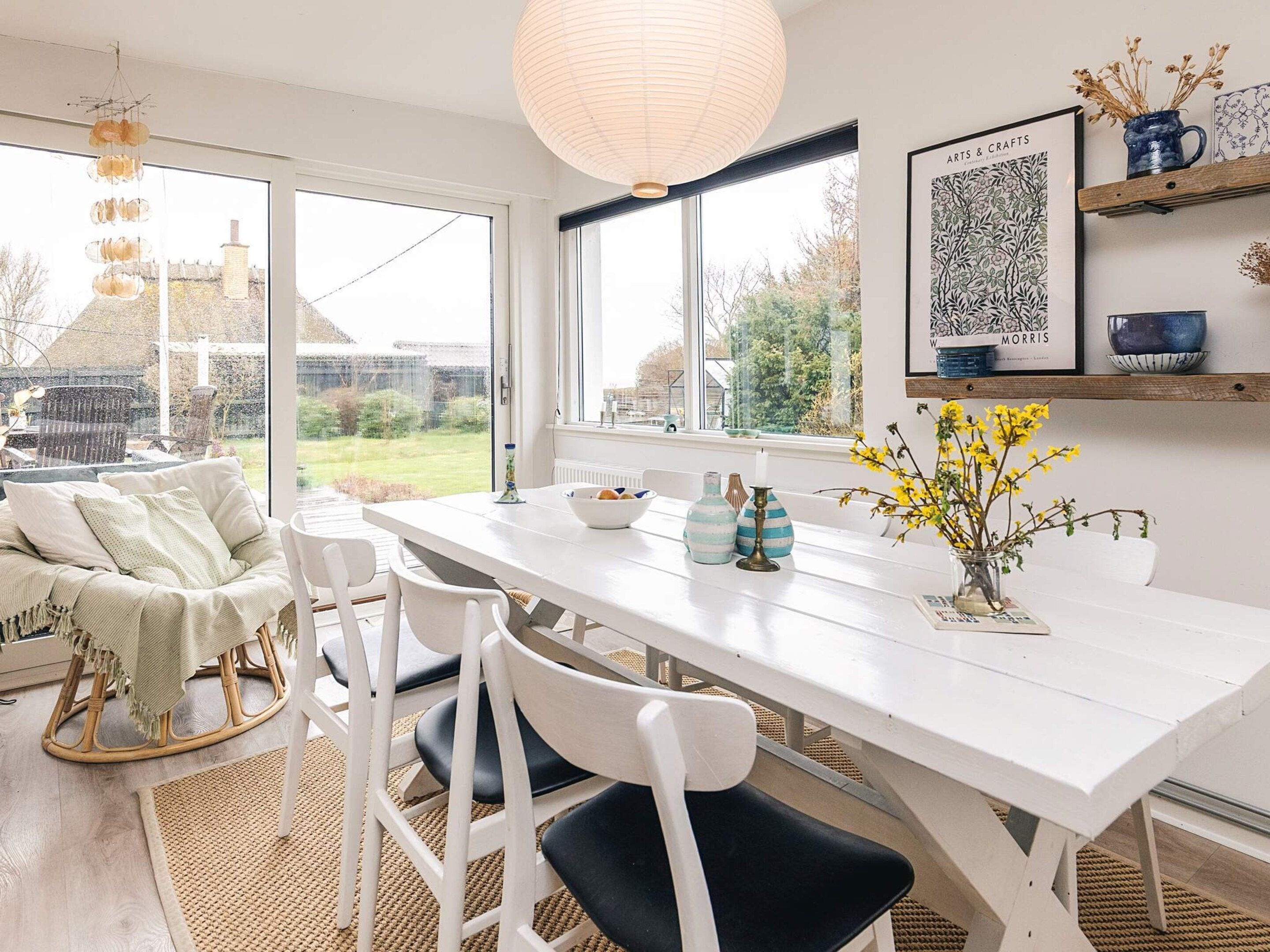 A bright kitchen with a white table, chairs, and a hanging light fixture.
