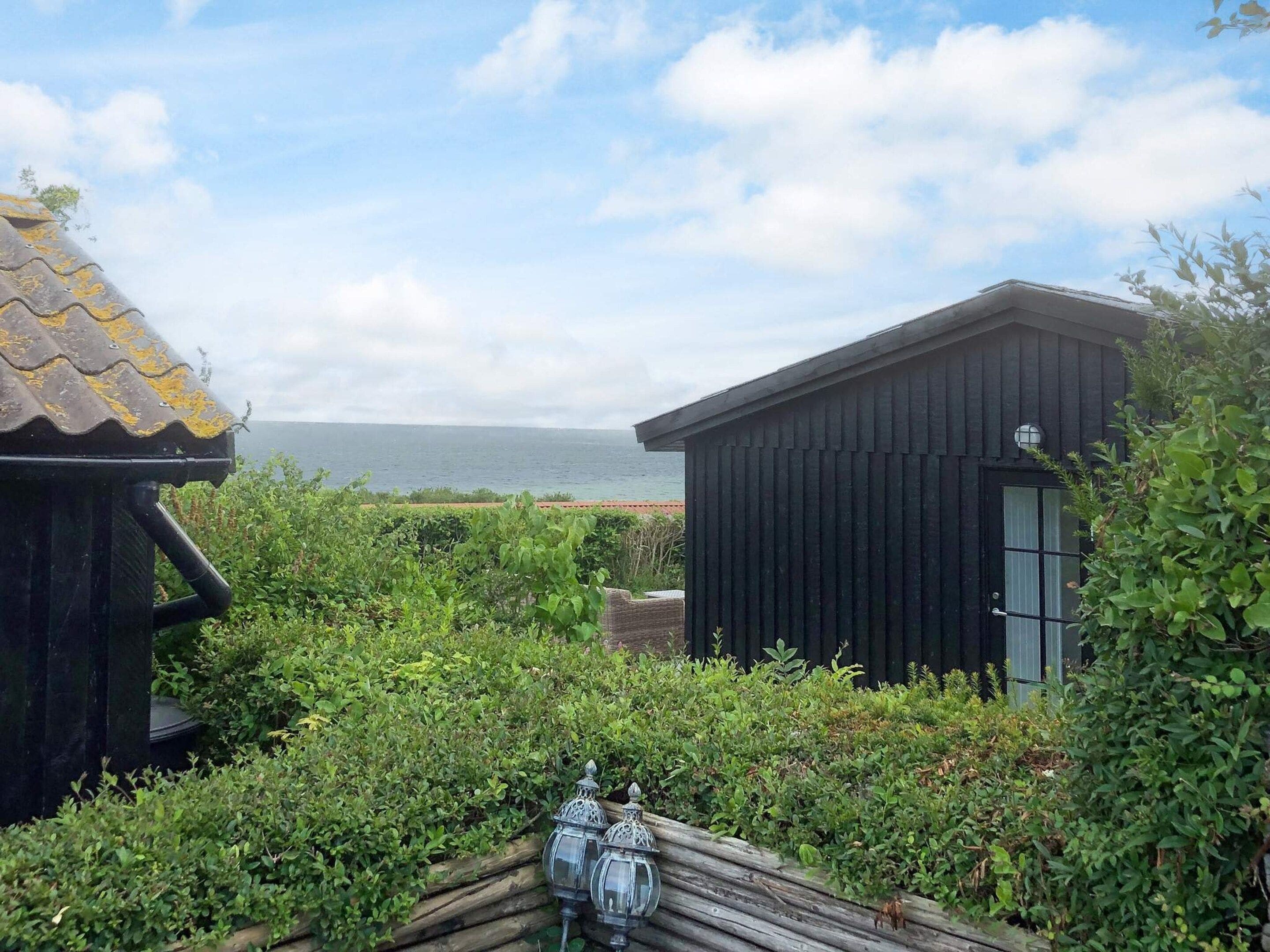 Eine Küstenimmobilie mit Holzbau und einem schwarzen Gebäude, umgeben von üppiger Vegetation mit Blick aufs Meer.
