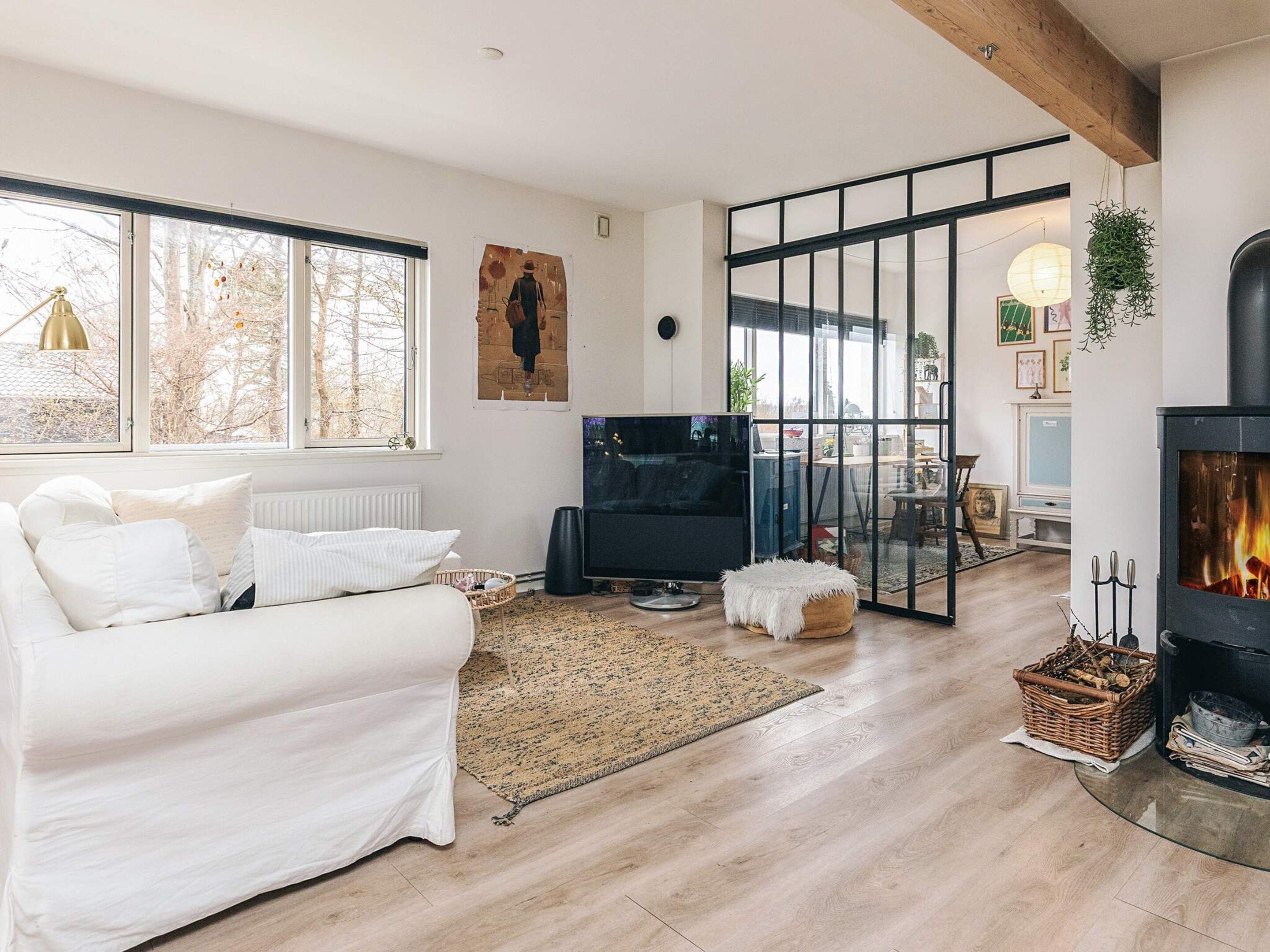 A modern living room with a sofa, TV, fireplace, and large windows.
