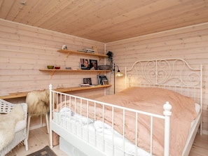 Ein Schlafzimmer mit einem weißen Metallbettgestell, einem weißen Stuhl und Holzregalen mit Büchern und Dekorationsgegenständen.