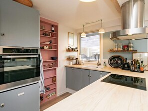 Cozinha moderna com forno embutido, estante rosa, janela com vista e exaustor de aço inoxidável.