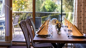 Une table à manger pour deux personnes, avec des chaises, donnant sur un paysage montagneux grâce à de grandes fenêtres, et un balcon.