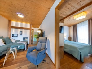 A modern hotel room with a wooden ceiling, a sofa, a chair, a bed, and a television.