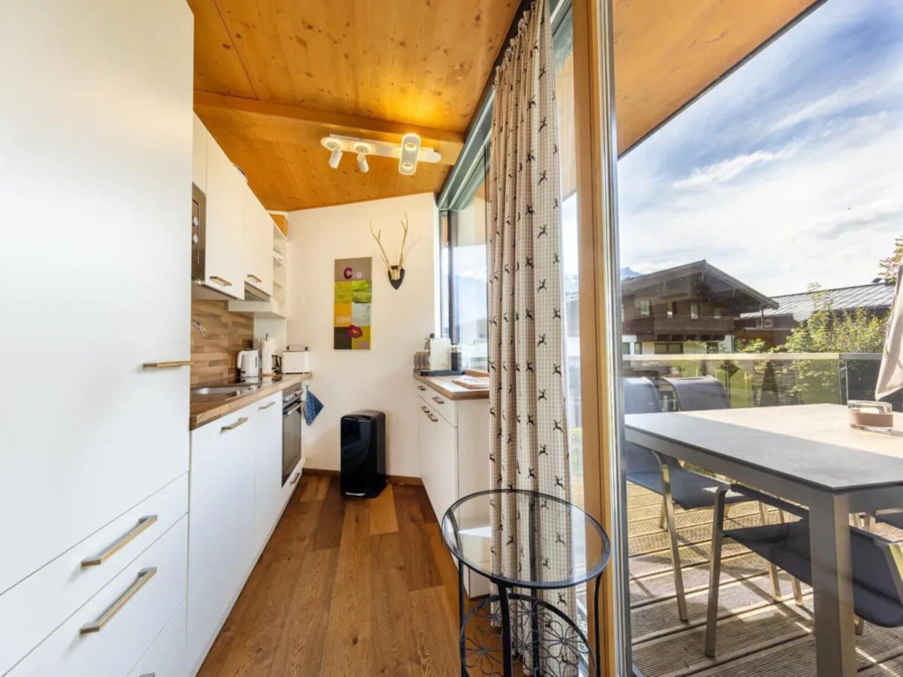 Eine kompakte Küche mit Holzboden, ein Essbereich mit Tisch und Stühlen sowie ein Blick ins Freie.
