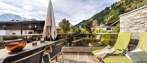 Une terrasse en bois avec des meubles d’extérieur, une table sur laquelle se trouve un saladier, et un mur en pierre.