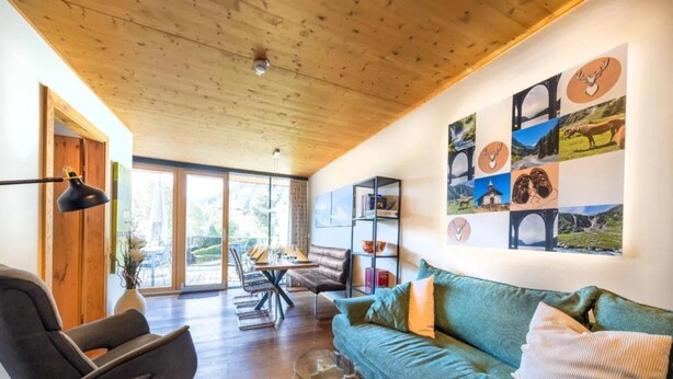 Un salon moderne avec un canapé vert, une table basse en verre et un plafond en bois.