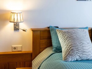 Een bed met een geborduurde blauwe deken, een gestructureerd kussen en een aan de muur bevestigde lamp.