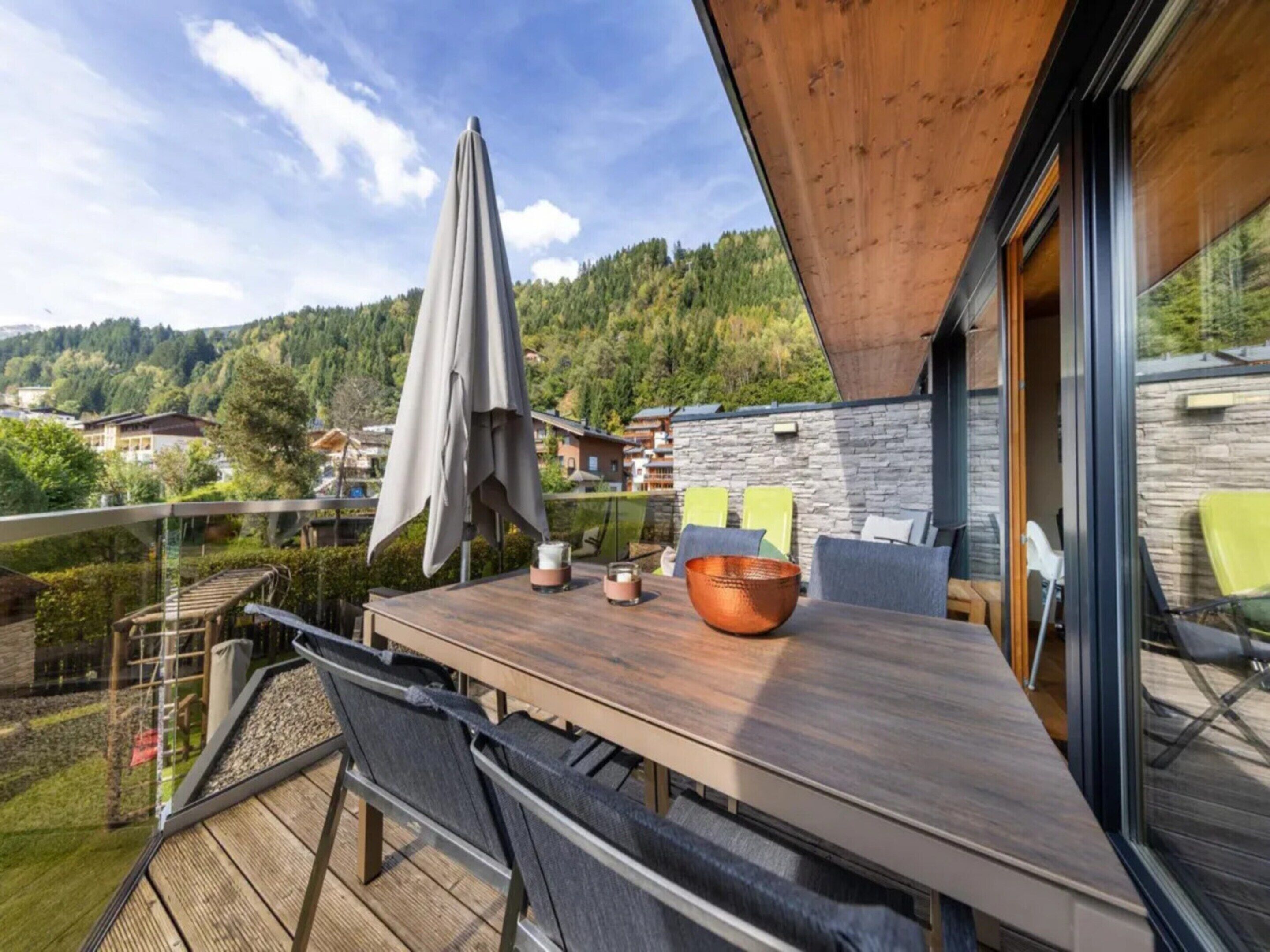 Un espace extérieur aménagé pour les repas, avec une table en bois, des chaises et un grand parasol.