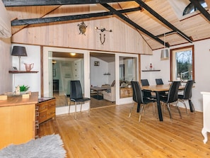 A spacious room with wooden flooring, a dining table with chairs, a desk with a lamp, and a large window. - Charming Cottage Near Forest in Farso (Farso)