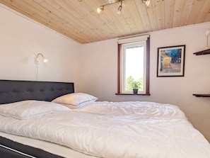 A bedroom with a bed, a window with a plant, a wall-mounted light, and a framed picture. - Charming Cottage Near Forest in Farso (Farso)