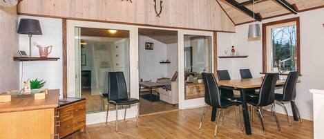 Una habitación amplia con suelo de madera, una mesa de comedor con sillas, un escritorio con lámpara y un ventanal grande.