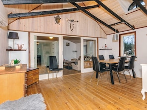 A spacious room with wooden flooring, a dining table with chairs, a desk with a lamp, and a large window. - 8 Person Holiday Home in Farso (Farso)