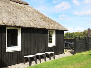 A thatched-roof cottage with two windows and a small outdoor seating area. - 8 Person Holiday Home in Farso (Farso)