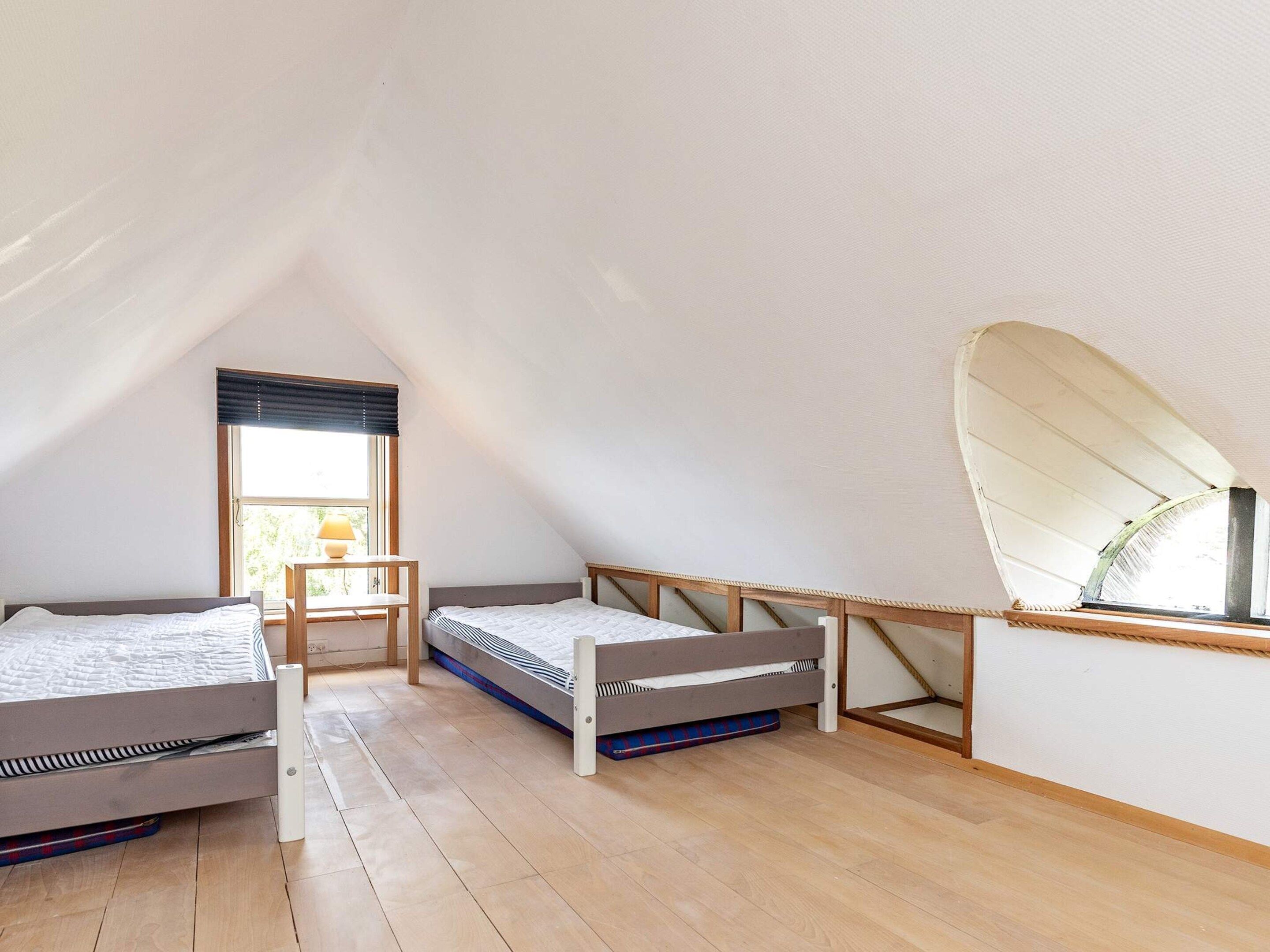 A small, triangular attic bedroom with two beds, a desk, and a window.