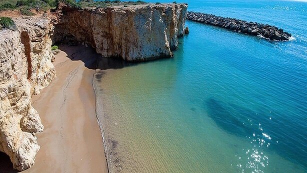 Una playa costera con un acantilado rocoso y mar tranquilo.