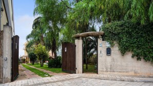 Una entrada protegida con un arco de concreto, un camino pavimentado y un muro con vegetación y un buzón.