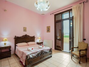 A bedroom with a large bed, two bedside tables with lamps, a chair, and a balcony door. - Pet-friendly Villa w/ Pool (Floridia)