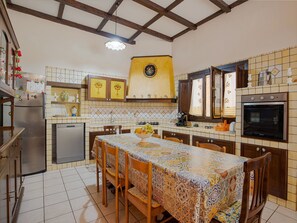 A kitchen with a tiled backsplash, wooden cabinets, a dining table with chairs, a refrigerator, a stove, and a sink. - Pet-friendly Villa w/ Pool (Floridia)