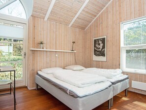 A bedroom with a bed, a shelf with a clock and a plant, and a framed picture on the wall. - Holiday Home in Ebeltoft (Ebeltoft)
