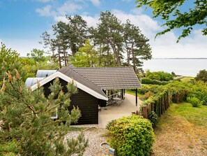 Eine Hütte mit geneigtem Dach, umgeben von Bäumen und Blick auf das Wasser.