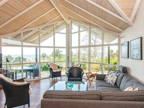 A spacious living area with a high ceiling and large windows offering a view of the outdoors.
