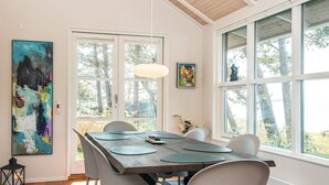 A dining area with a large table, chairs, and a view of trees through large windows. - Holiday Home in Ebeltoft (Ebeltoft)