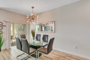 A dining area with a glass table and chairs, a modern chandelier, and a large mirror on the wall. - "Pequod Lakeview" - 4BD/3BA Townhome near Disney (Kissimmee)