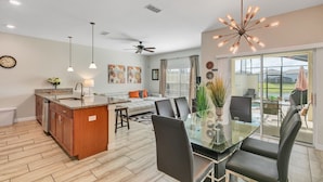 A modern kitchen with a central island, dining area with glass table and chairs, and a large sliding glass door to a patio. - "Pequod Lakeview" - 4BD/3BA Townhome near Disney (Kissimmee)