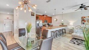 A modern kitchen with a central island, a dining area with a glass table, and a living room with a sofa and a ceiling fan. - "Pequod Lakeview" - 4BD/3BA Townhome near Disney (Kissimmee)