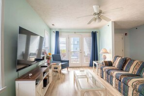 Ein Wohnzimmer mit Flachbildfernseher, einer Couch, einem Couchtisch und einem Deckenventilator.