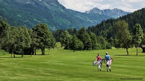 Een golfbaan met een bergachtige achtergrond, bomen en een heldere lucht.