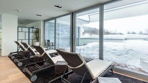 Een moderne binnenruimte met grote ramen, een zithoek met stoelen en tafels, en zicht op een besneeerd landschap.
