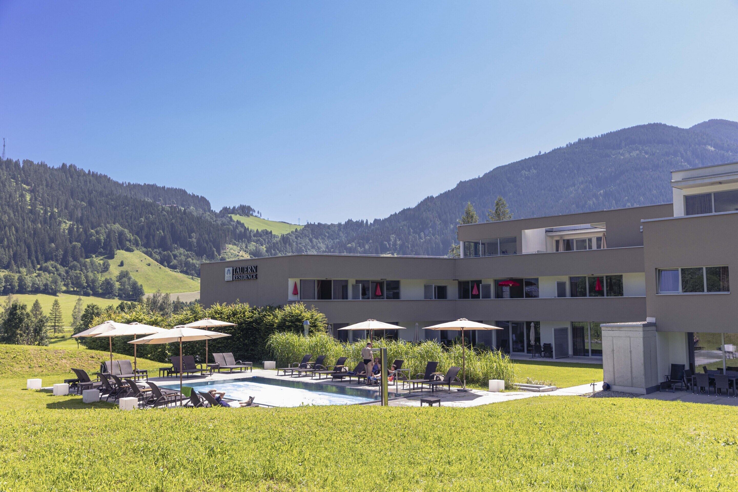 A hotel with a swimming pool, outdoor seating, and a view of mountains.