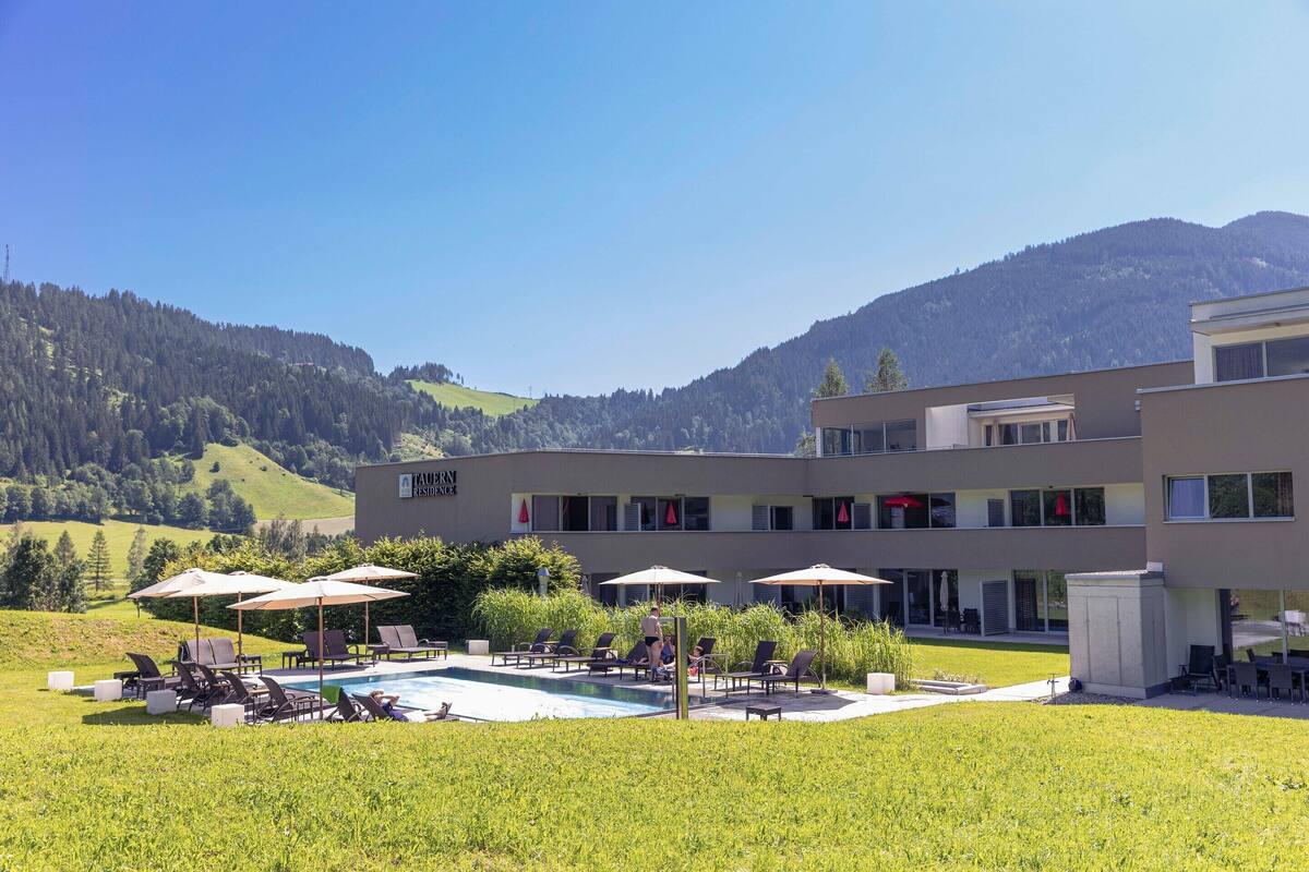 Ein Hotel mit Poolbereich, Außenbereich zum Sitzen und Blick auf Berge.