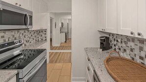 A modern kitchen with white cabinetry, a microwave, an oven, a coffee maker, and a woven basket. - Modern Twist in Historic Building, sleeps 6 (Atlanta)