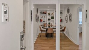 A modern hallway with wooden flooring, a dining area with a round table and chairs, and a mirrored wall reflecting the room. - Modern Twist in Historic Building, sleeps 6 (Atlanta)