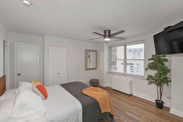 A bedroom with a bed, a ceiling fan, a window with blinds, a radiator, and a potted plant.