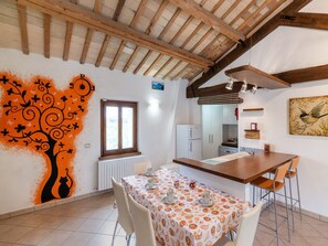 A dining area with a table set for four, a window, a radiator, and a kitchen in the background. - Holiday House in Filottrano on the Beach by the sea (Filottrano)