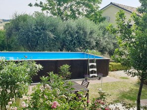 A swimming pool with a ladder, surrounded by lush greenery and a patio area with a table and chairs. - Holiday House in Filottrano on the Beach by the sea (Filottrano)